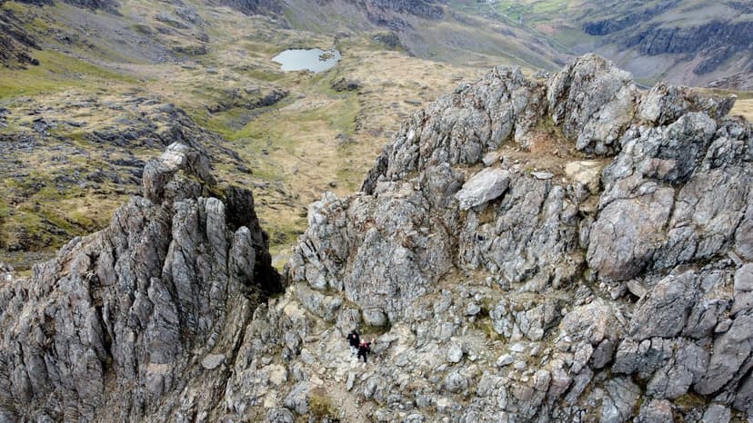 Scramblers on rocky arete ridge in Snowdonia with mountain tarn below