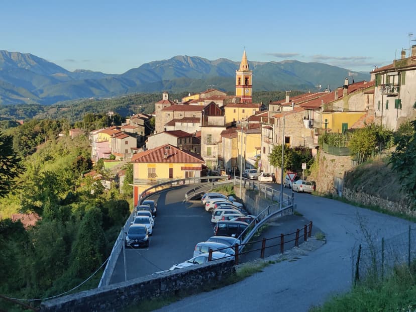 Garfagnana hill village with buildings, parked cars, and mountain ridge backdrop