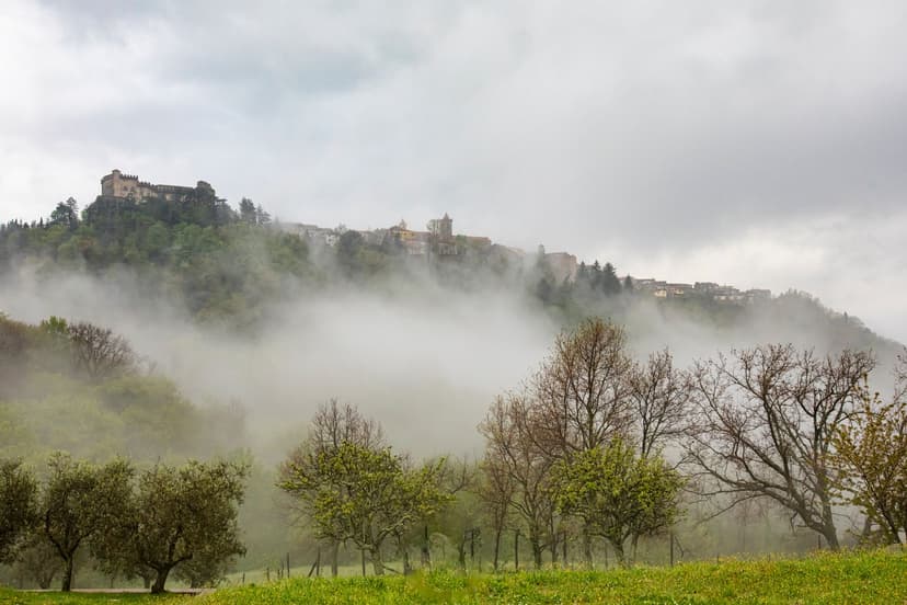 Fosdinovo Castle on a hill shrouded in mist in Lunigiana with surrounding trees