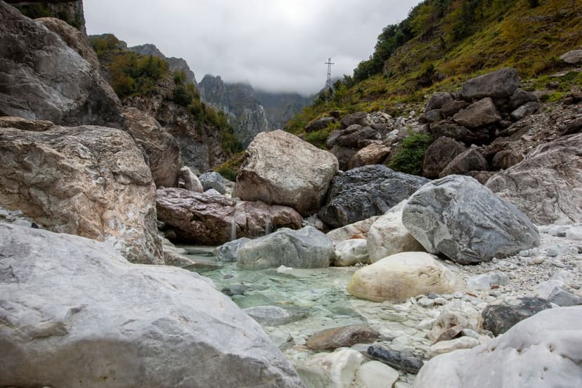 Apuan Alps Carrara marble peaks and rocky riverbed with clear water under cloudy sky
