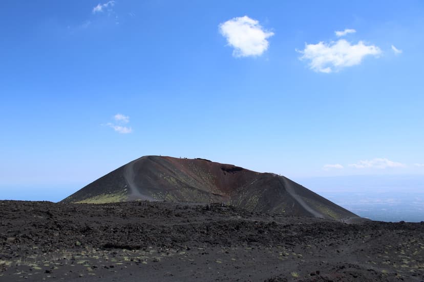 Mount Etna crater cone and dark volcanic lava field in Sicily under blue sky