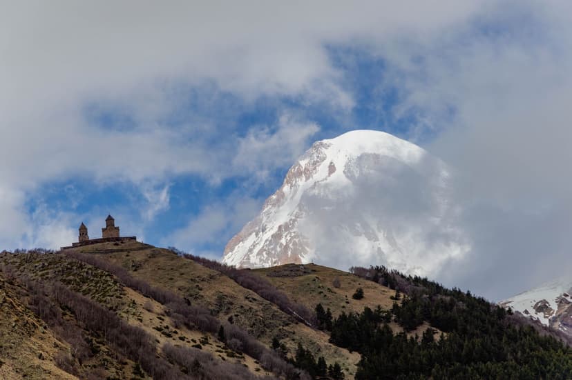 Gergeti Trinity Church on a hill with Mount Kazbek in the background under cloudy skies