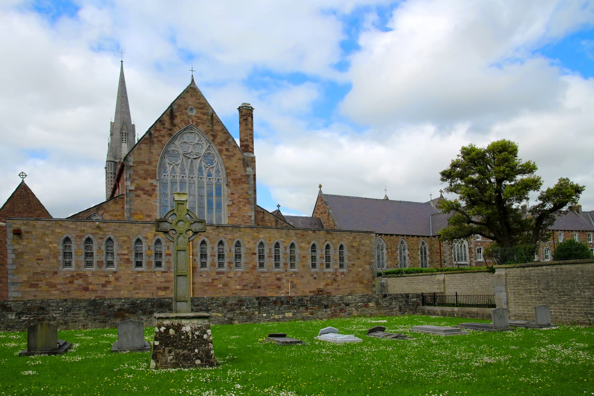 Stone Celtic cross in graveyard before Tralee church under cloudy sky