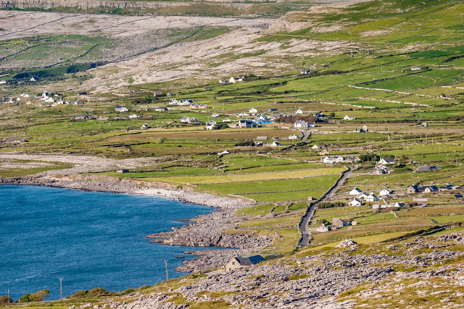 Coastal view of Ballyvaughan with green fields, stone walls, houses, and blue sea.