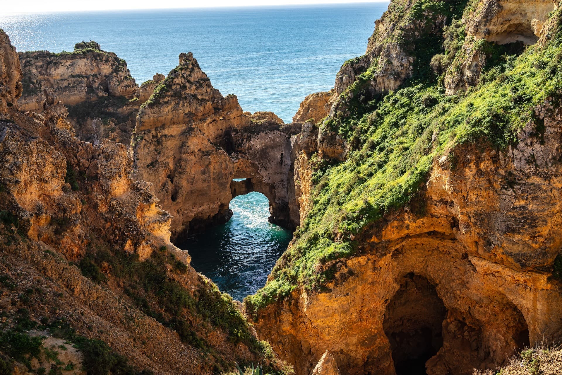 Coastal rock formations with sea arches and grottos overlooking the bright blue ocean.