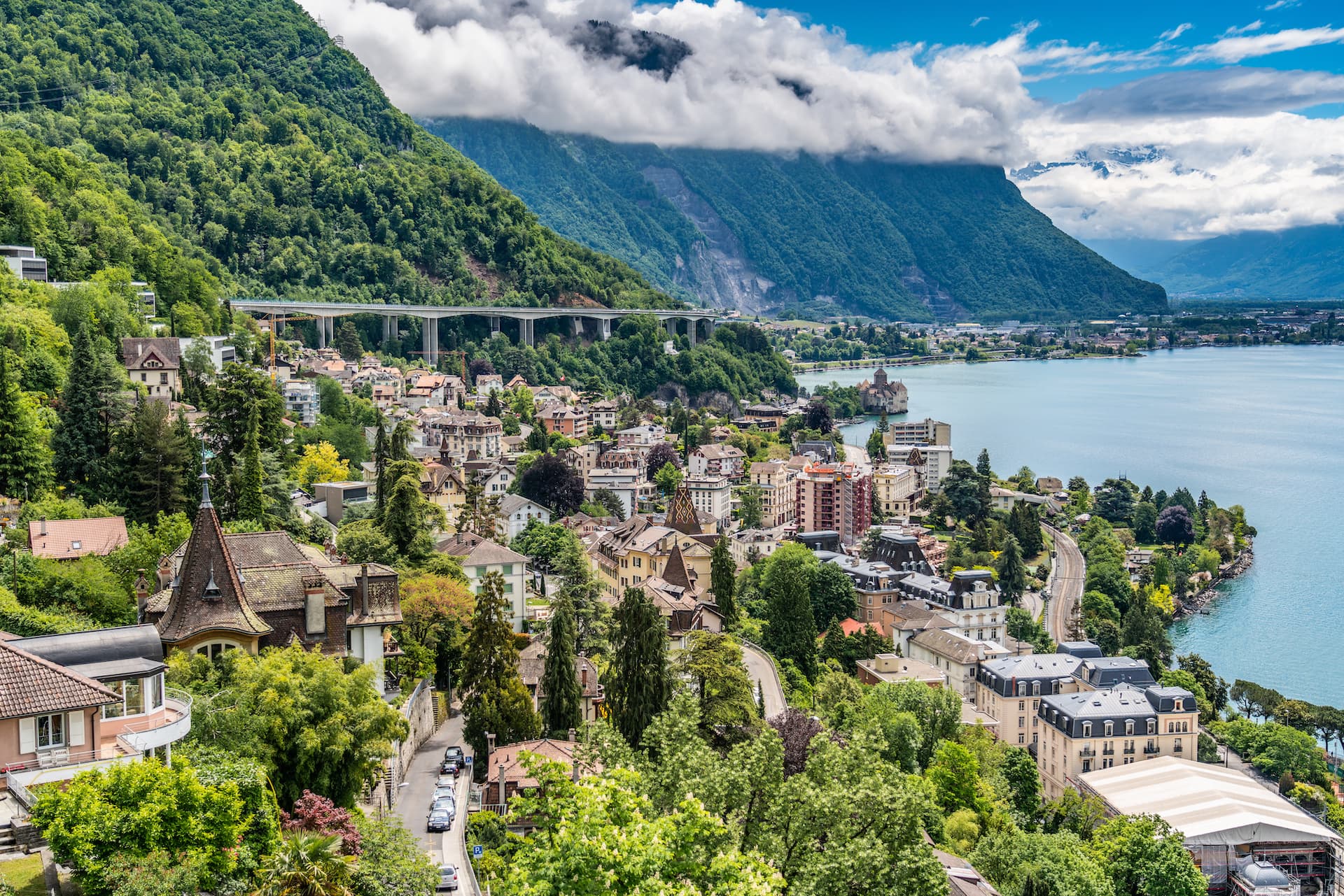 Montreux town nestled between steep green mountains and Lake Geneva with Chillon Castle visible.