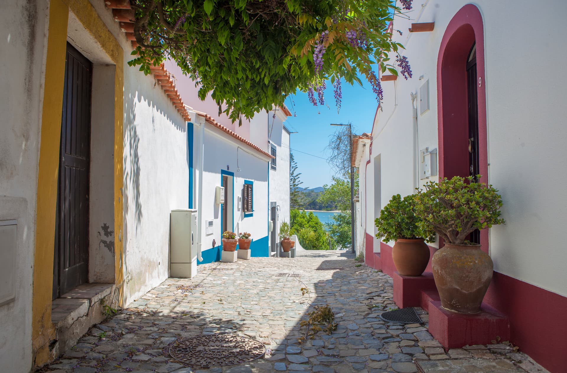 Cobblestone street in Vila Nova de Milfontes, Portugal, leading to a view of the sea.