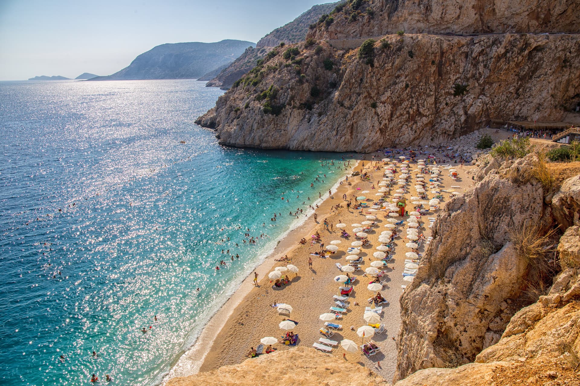 Crowded beach with sunbathers and swimmers near steep cliffs on the Mediterranean coastline near Antalya.