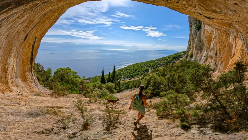 Hiker with backpack and dog walking out of a coastal cave toward the sea