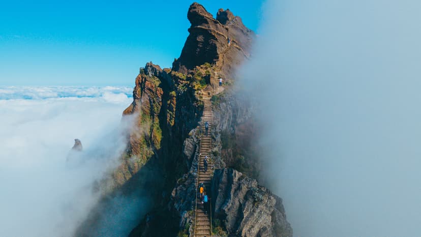 Hikers on steep mountain ridge stairs above a sea of clouds