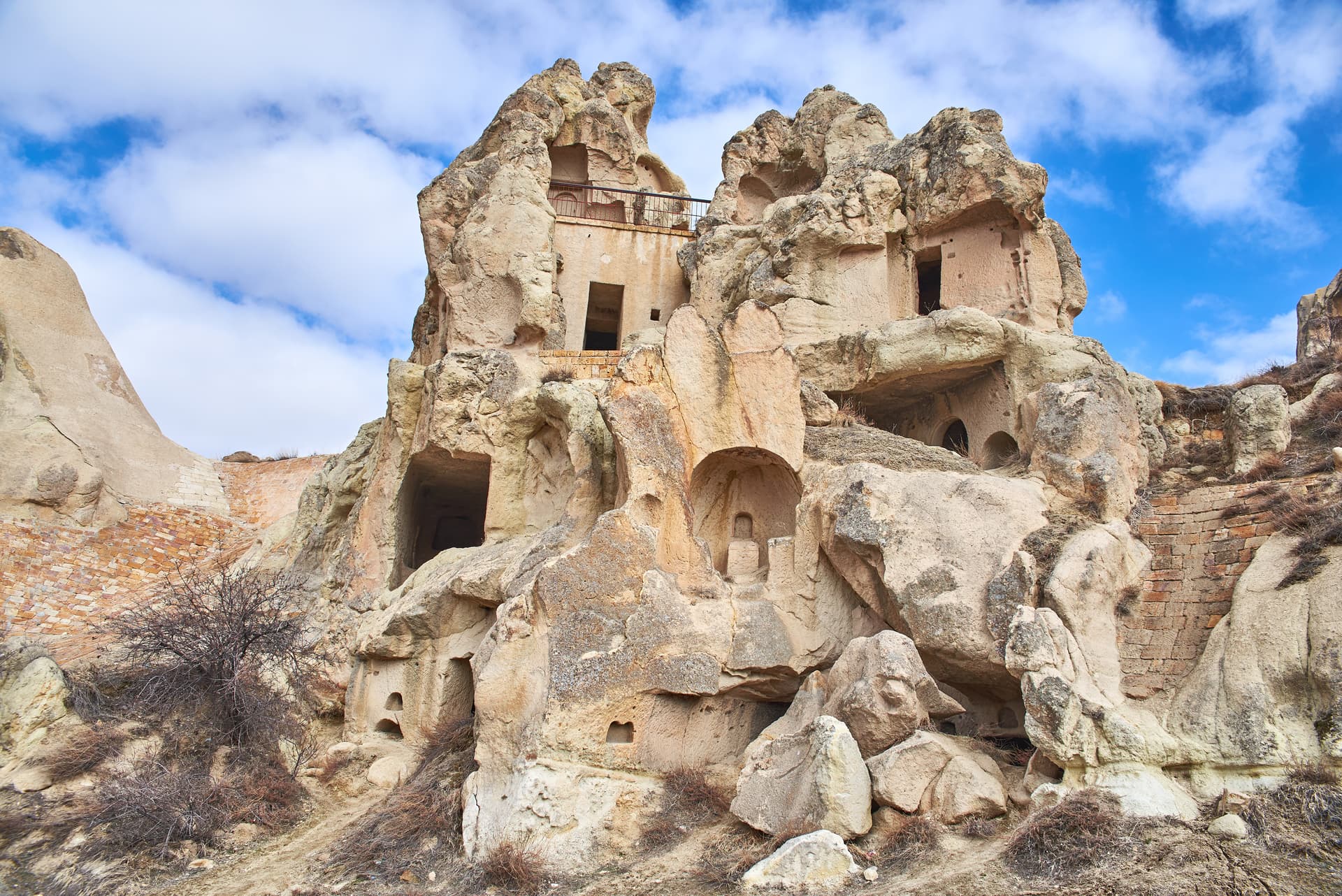 Cave dwellings carved into rock formations under a bright blue sky with white clouds in Göreme.
