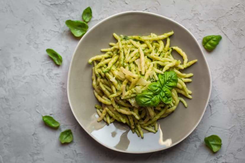 Pasta with green pesto sauce and basil leaves on gray plate