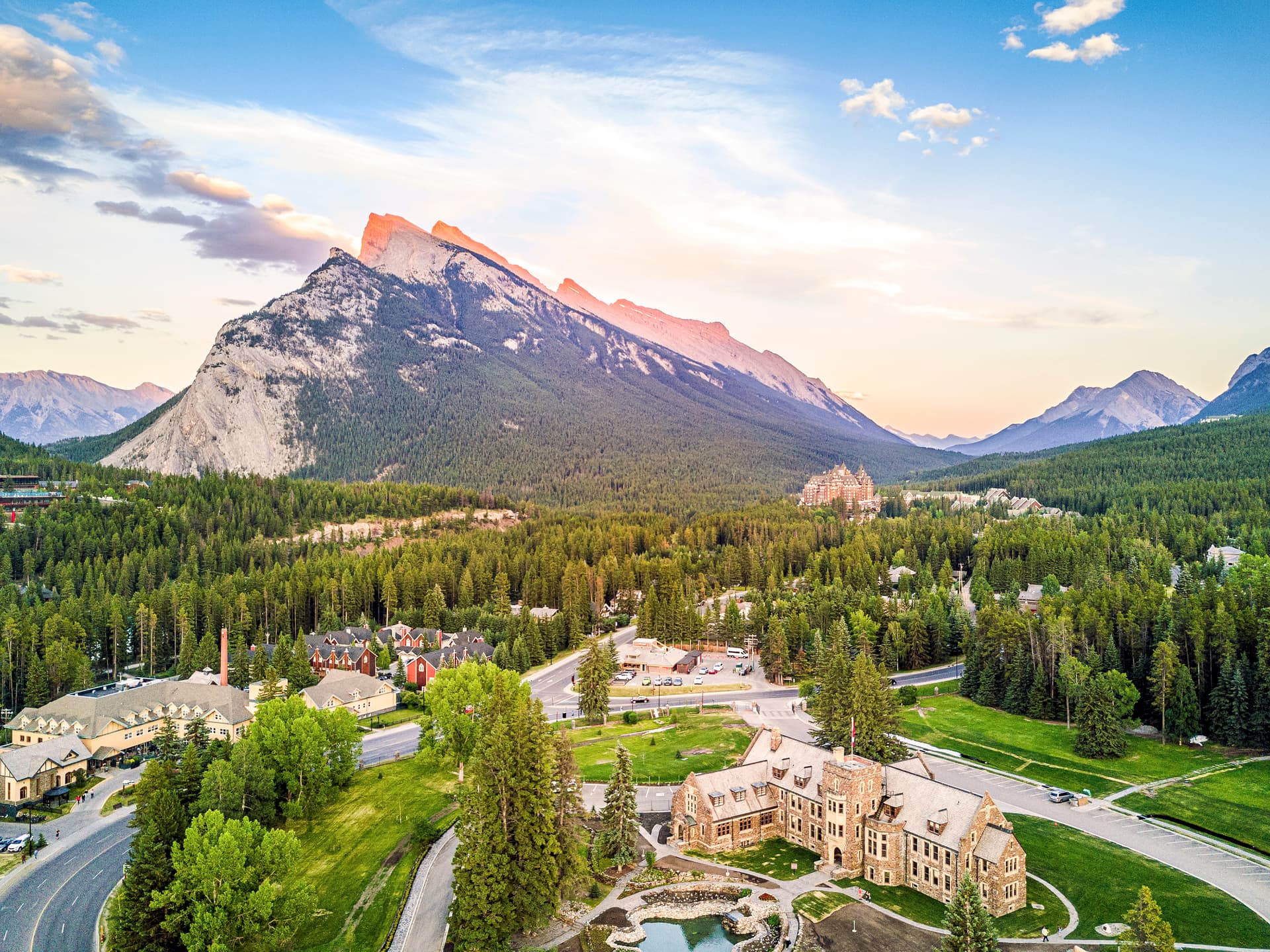 Aerial view of Banff townsite with mountain peaks at sunset and dense pine forest.