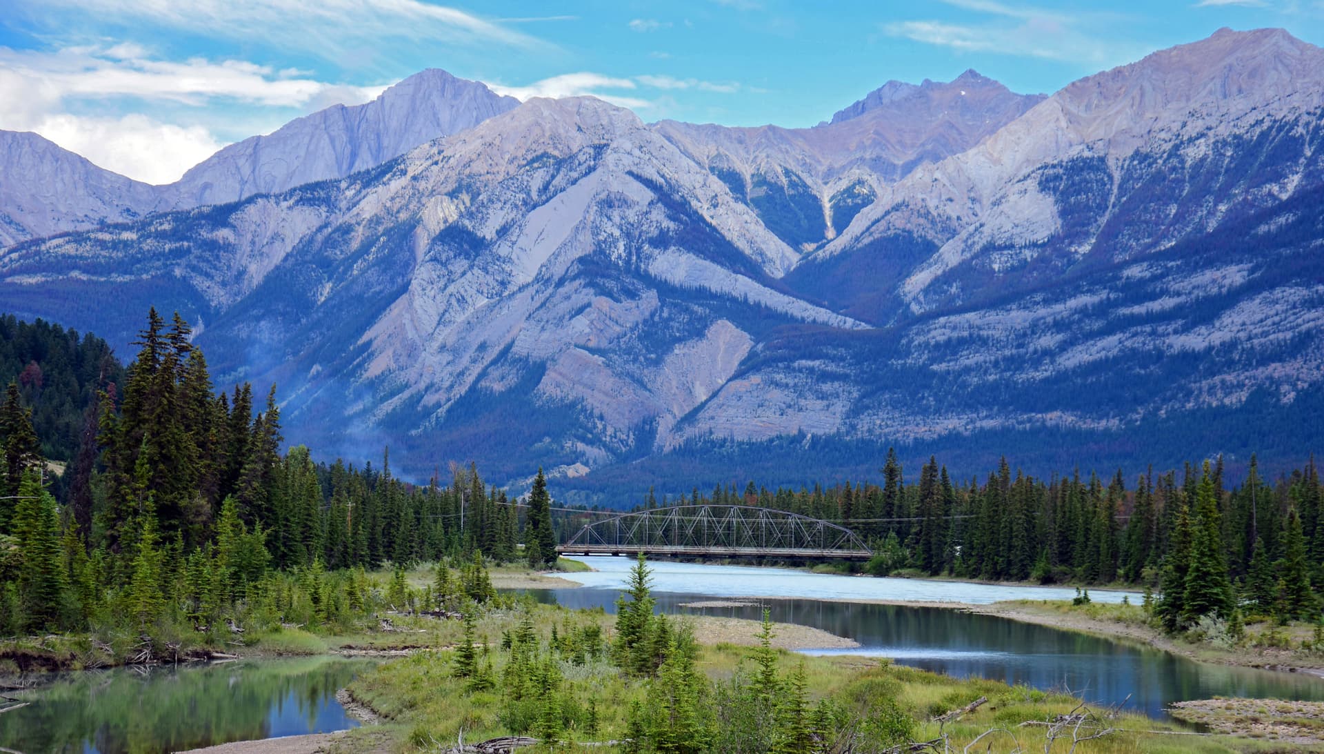 River flowing below large, rugged mountains with a steel truss bridge crossing the water.