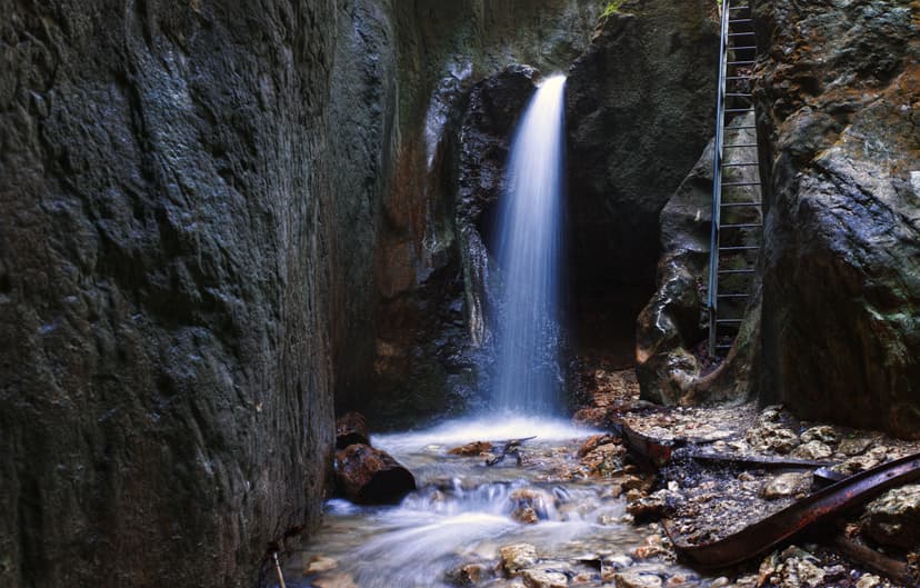 Waterfall flowing between narrow rock canyon walls with metal ladder