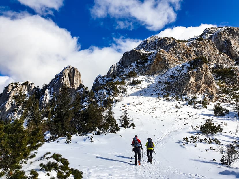 Hikers climbing snow-covered mountain with rocky peaks and blue sky