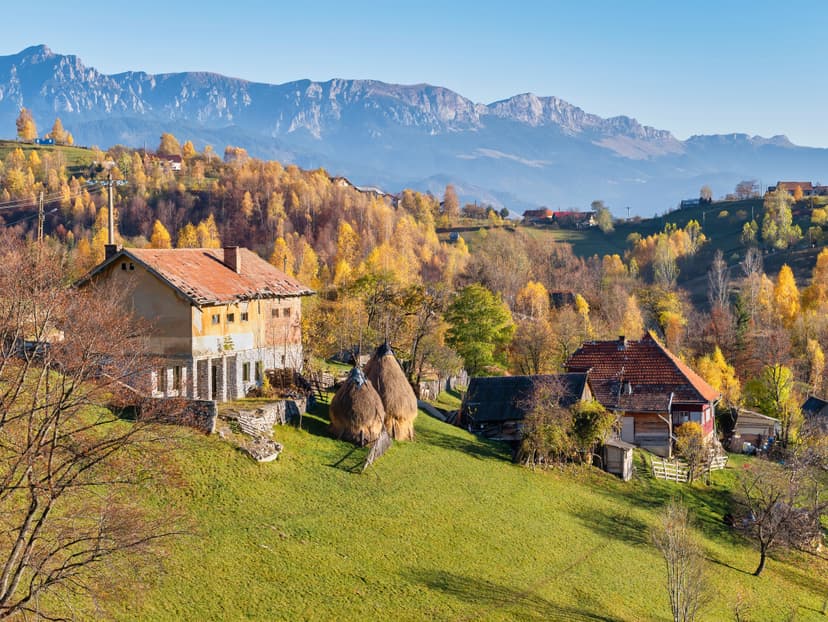 Rural mountain village with traditional houses and haystacks during autumn foliage under mountain range