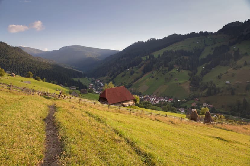 Hiking trail through green mountain valley with wooden barn and village