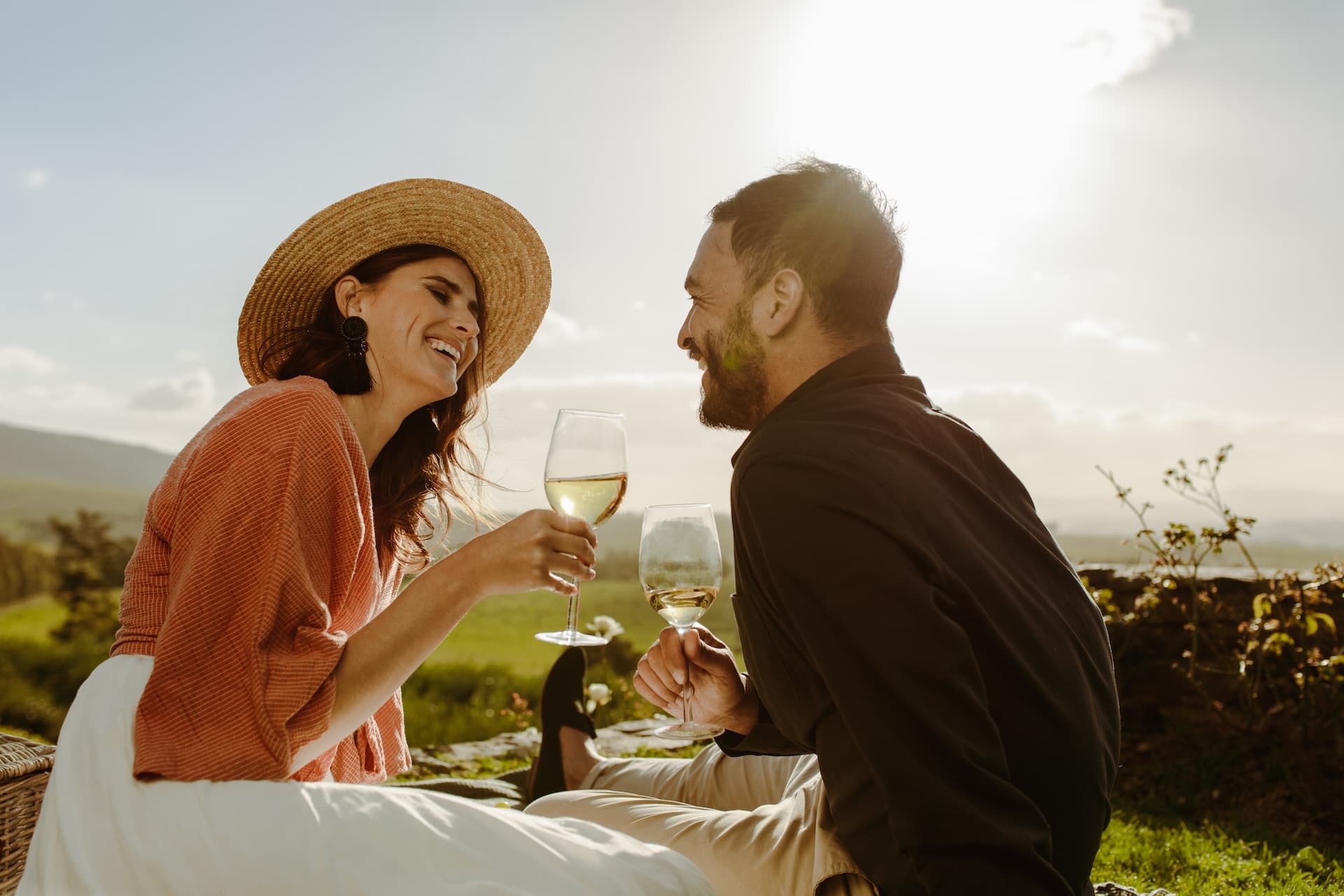 Couple toasting with white wine glasses near a vineyard on a sunny day