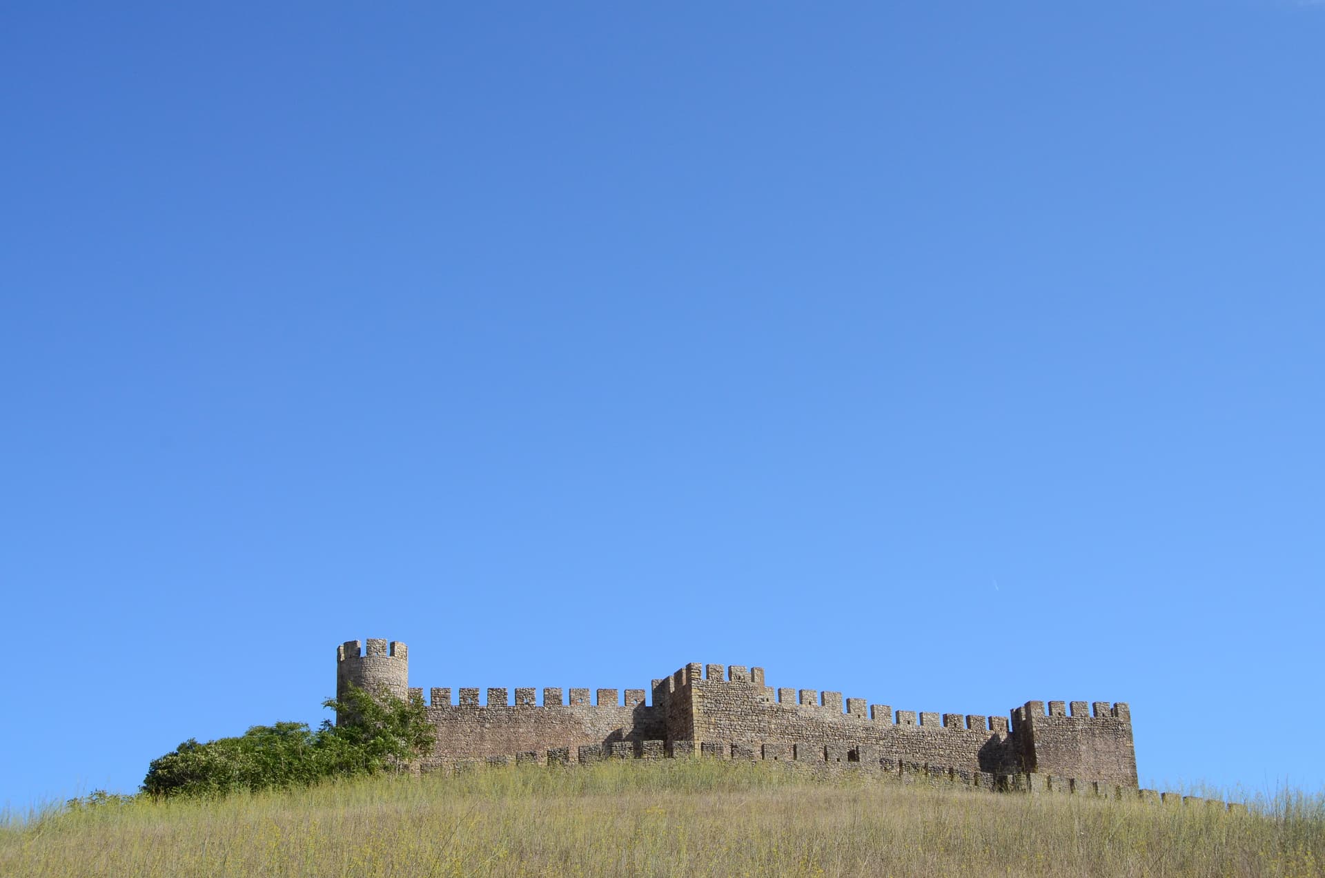Castelo de Santiago do Cacém stone fortress ruins atop a grassy hill under a clear blue sky.