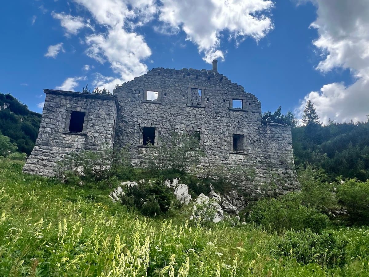 Stone ruins of an old building on a grassy mountain slope under a blue sky with clouds