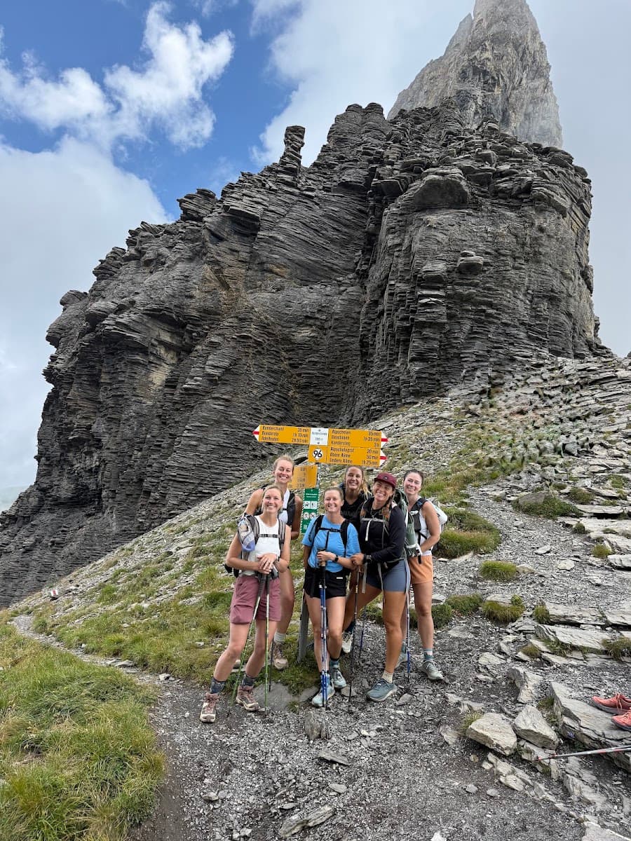 Group of hikers posing by trail sign in front of rocky mountain peak