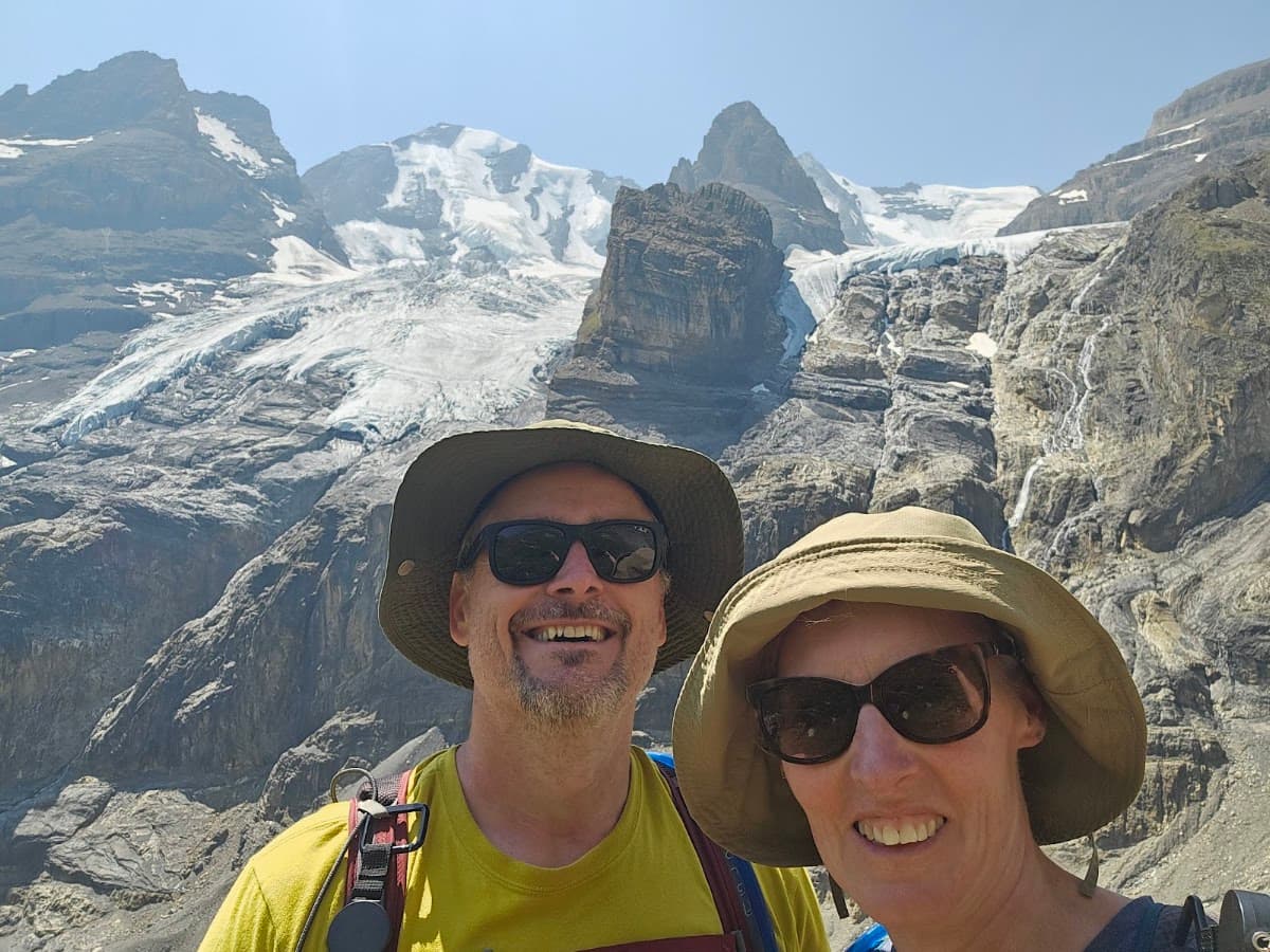 Hikers with hats and sunglasses in front of snowy mountain peaks and glacier