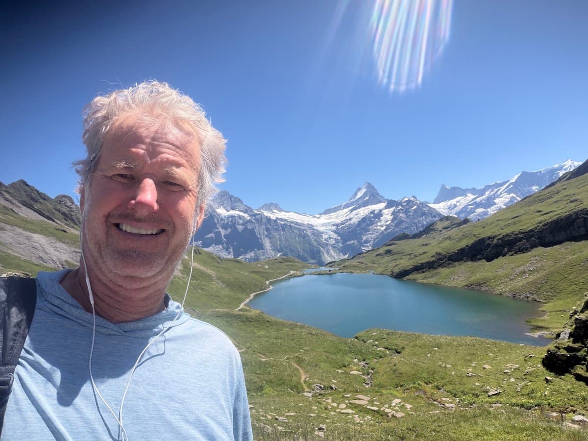 Hiker taking selfie in front of alpine lake and snow-capped mountain peaks