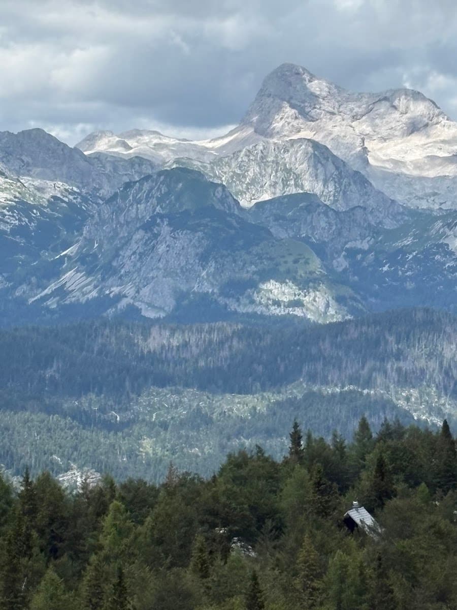 Alpine mountain peaks with rocky summits, forested slopes, and a small cabin roof visible below.