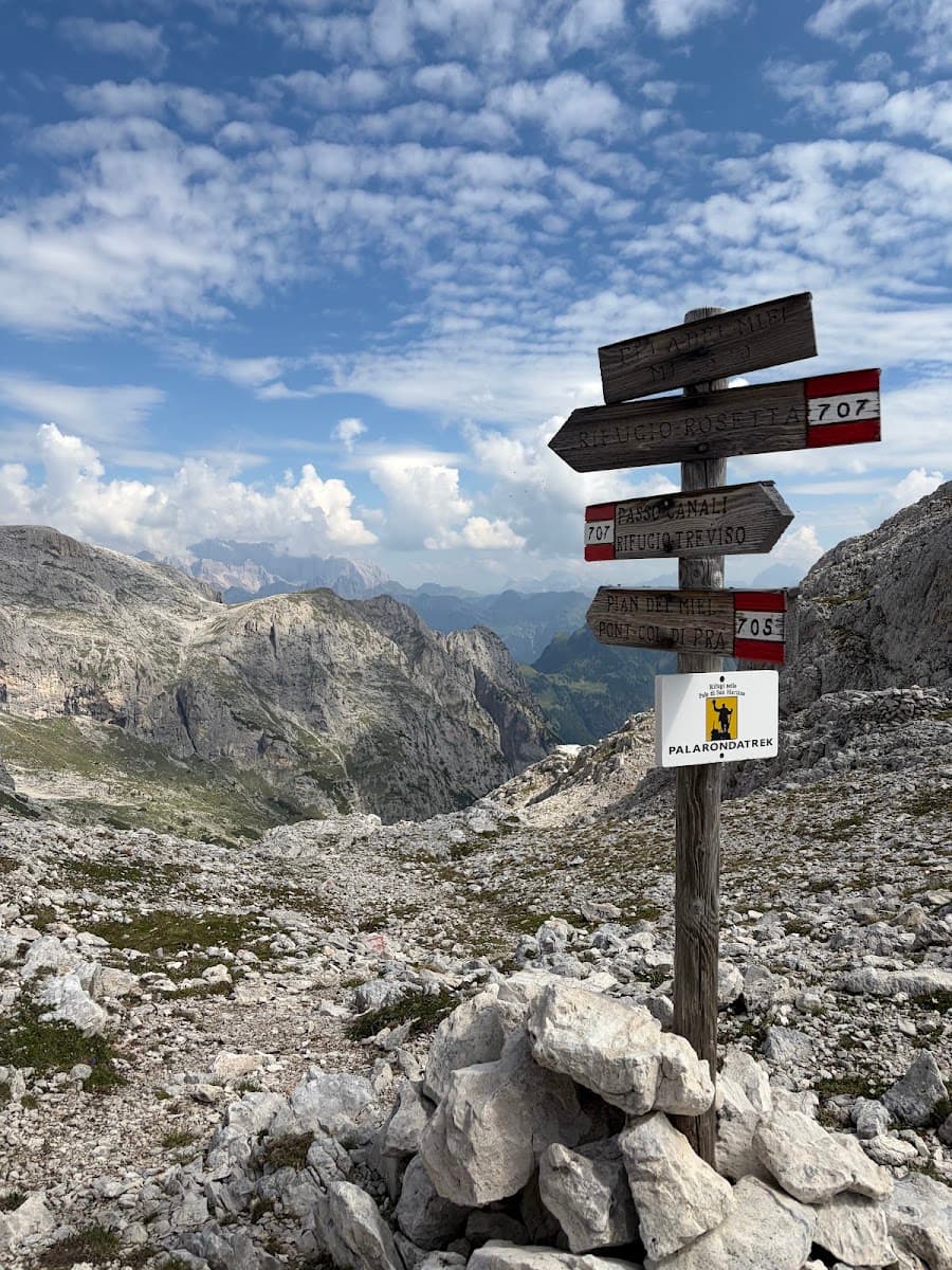 Wooden hiking trail signpost in rocky alpine mountain landscape with cloudy sky