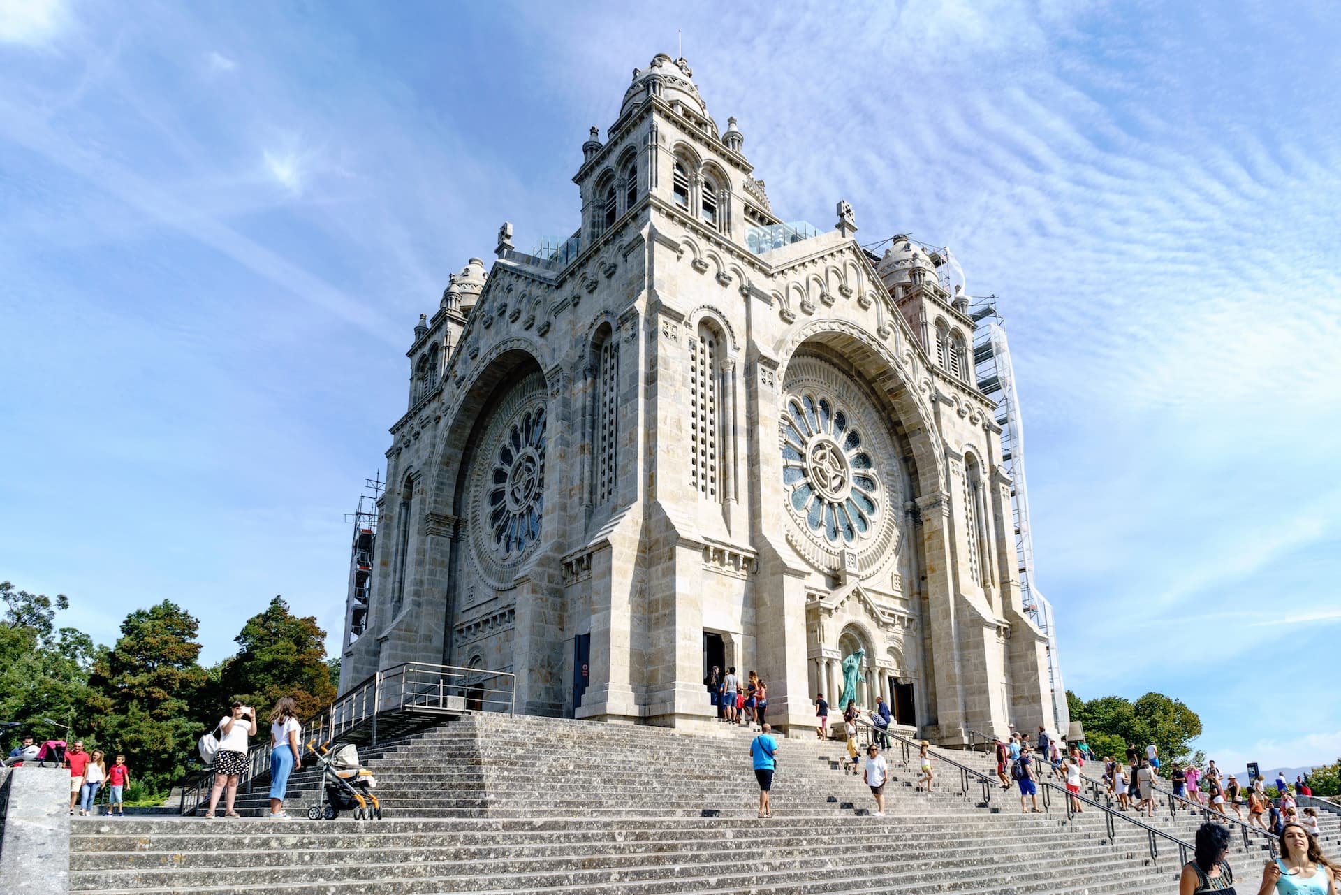 Monumental stone church with rose windows, approached by wide steps with many visitors in Viana do Castelo, Portugal.