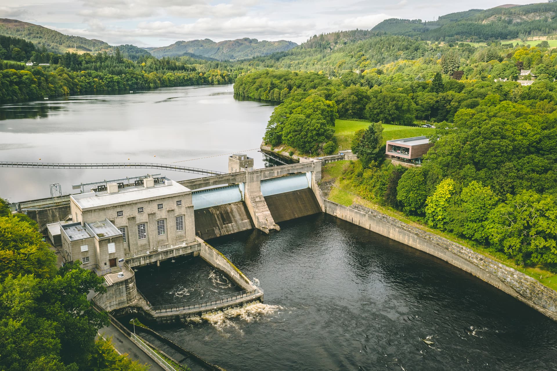Pitlochry Dam and power station releasing water into the river surrounded by lush green hills.