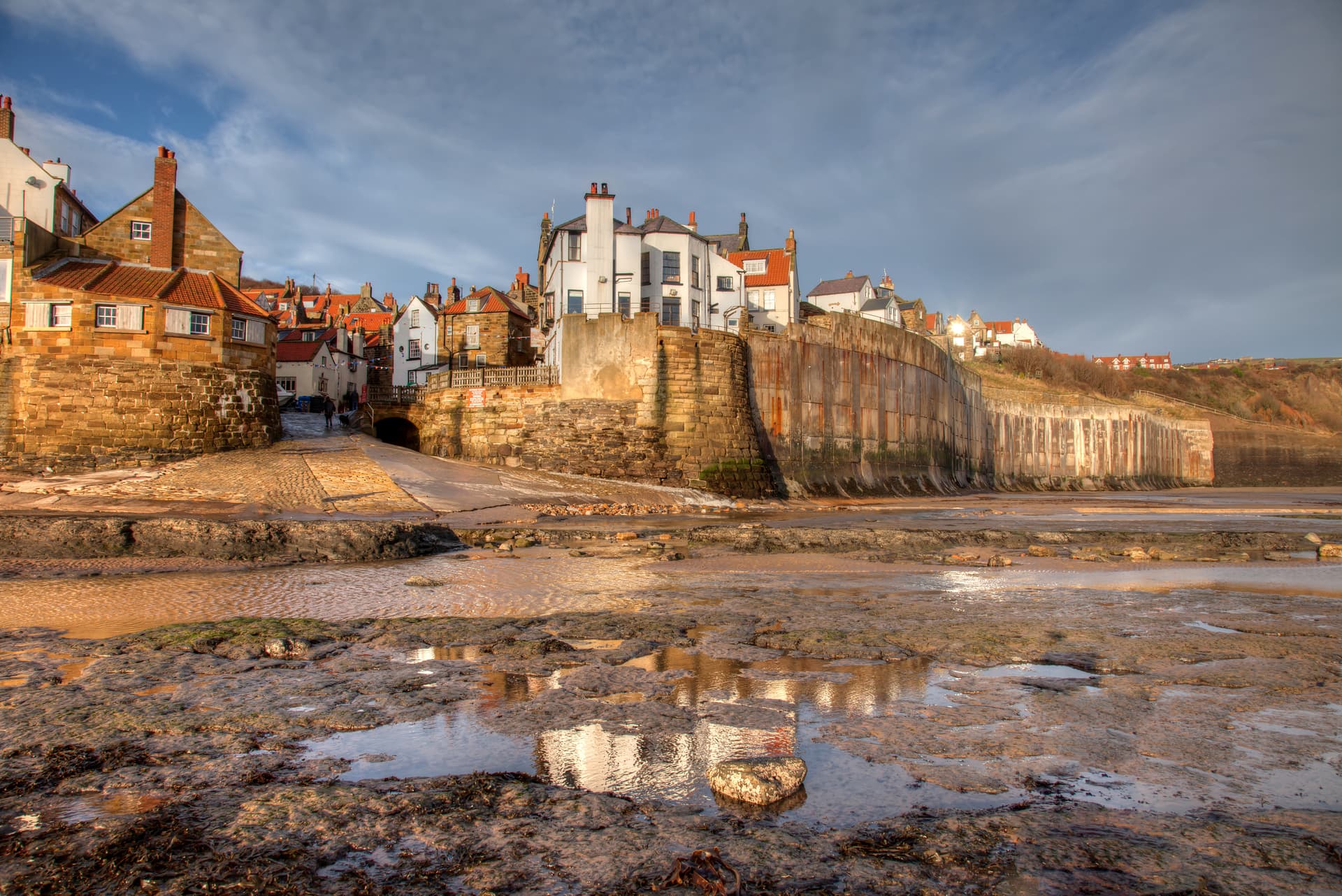 Coastal village houses above tidal mudflats with water reflections at Robin Hood's Bay.