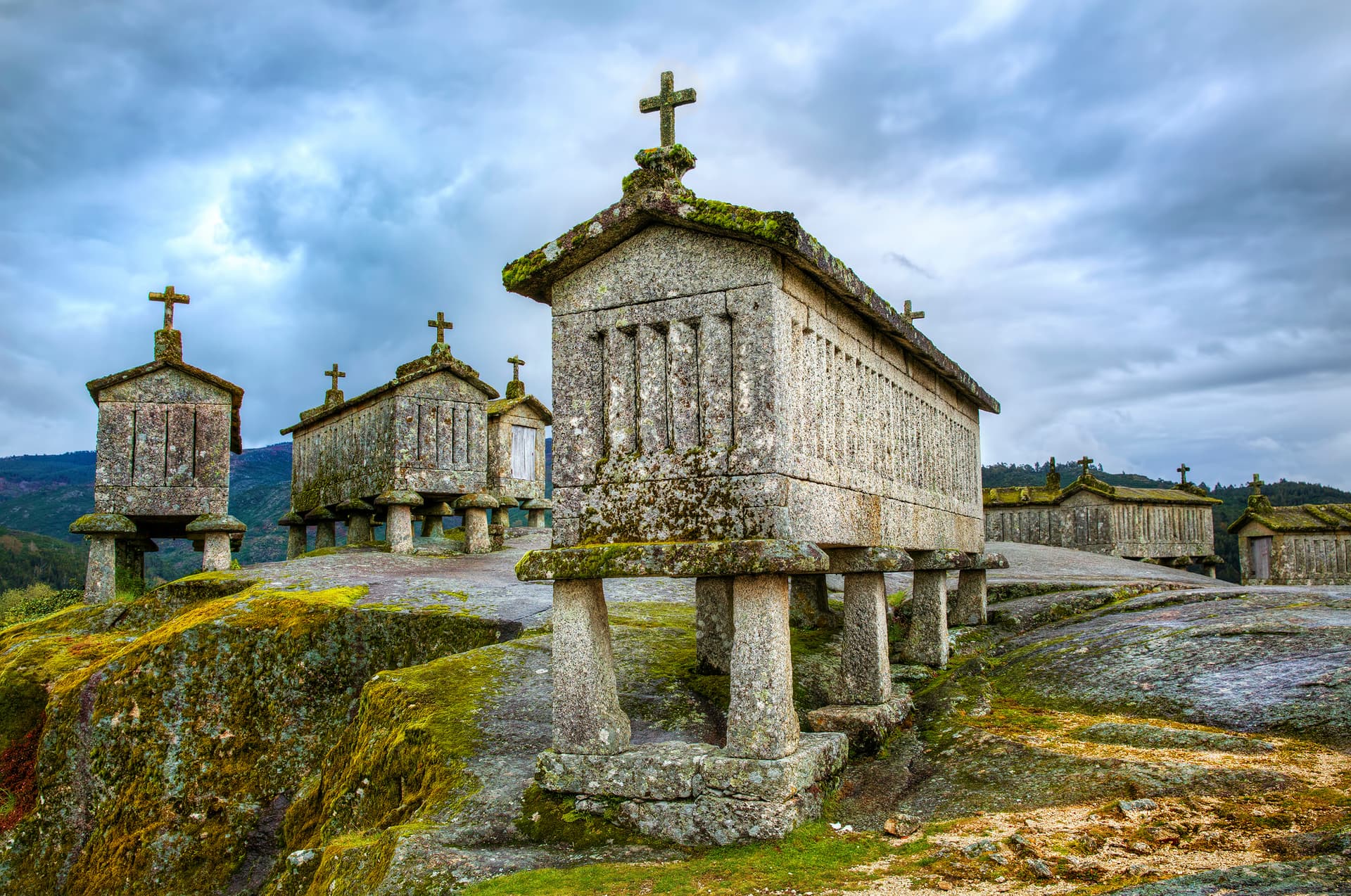 Stone granaries (espigueiros) with crosses atop, set on mossy rock under a cloudy sky in Soajo, north Portugal.