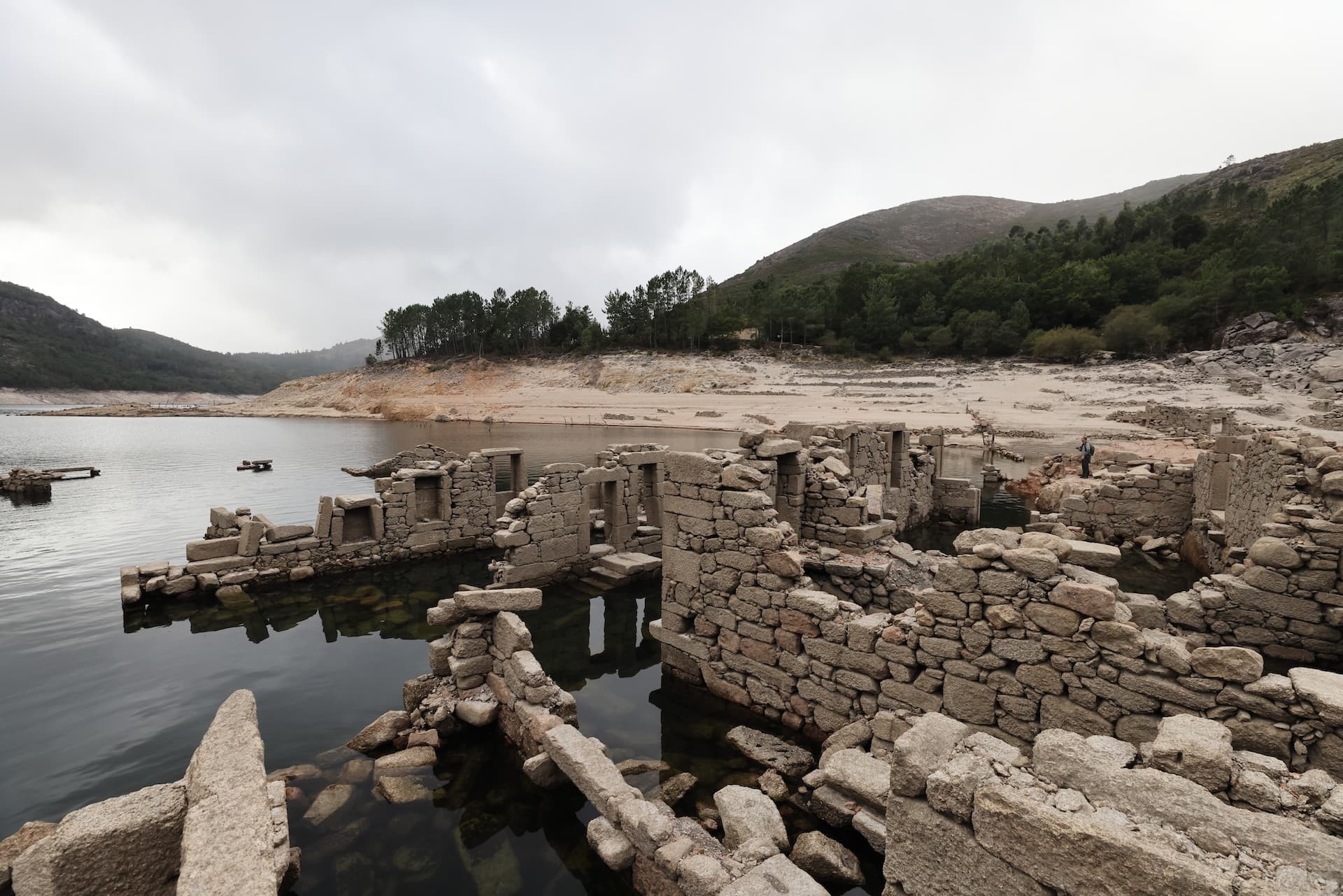 Stone ruins of Vilarinho da Furna partially submerged in low reservoir water during the dry season.