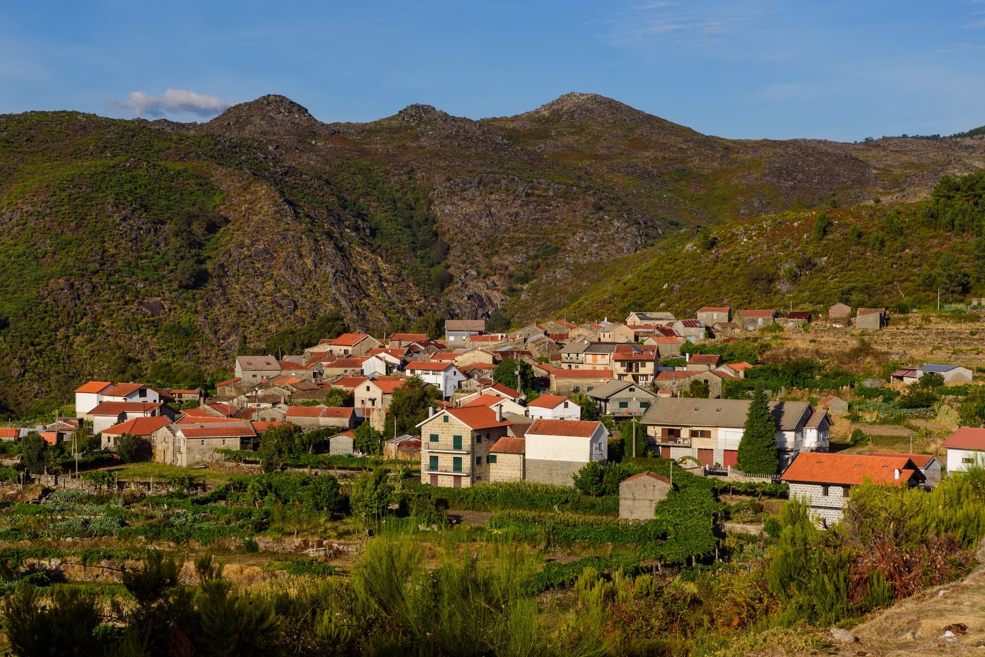 Village nestled in a valley with terraced fields below rugged, scrub-covered mountains.