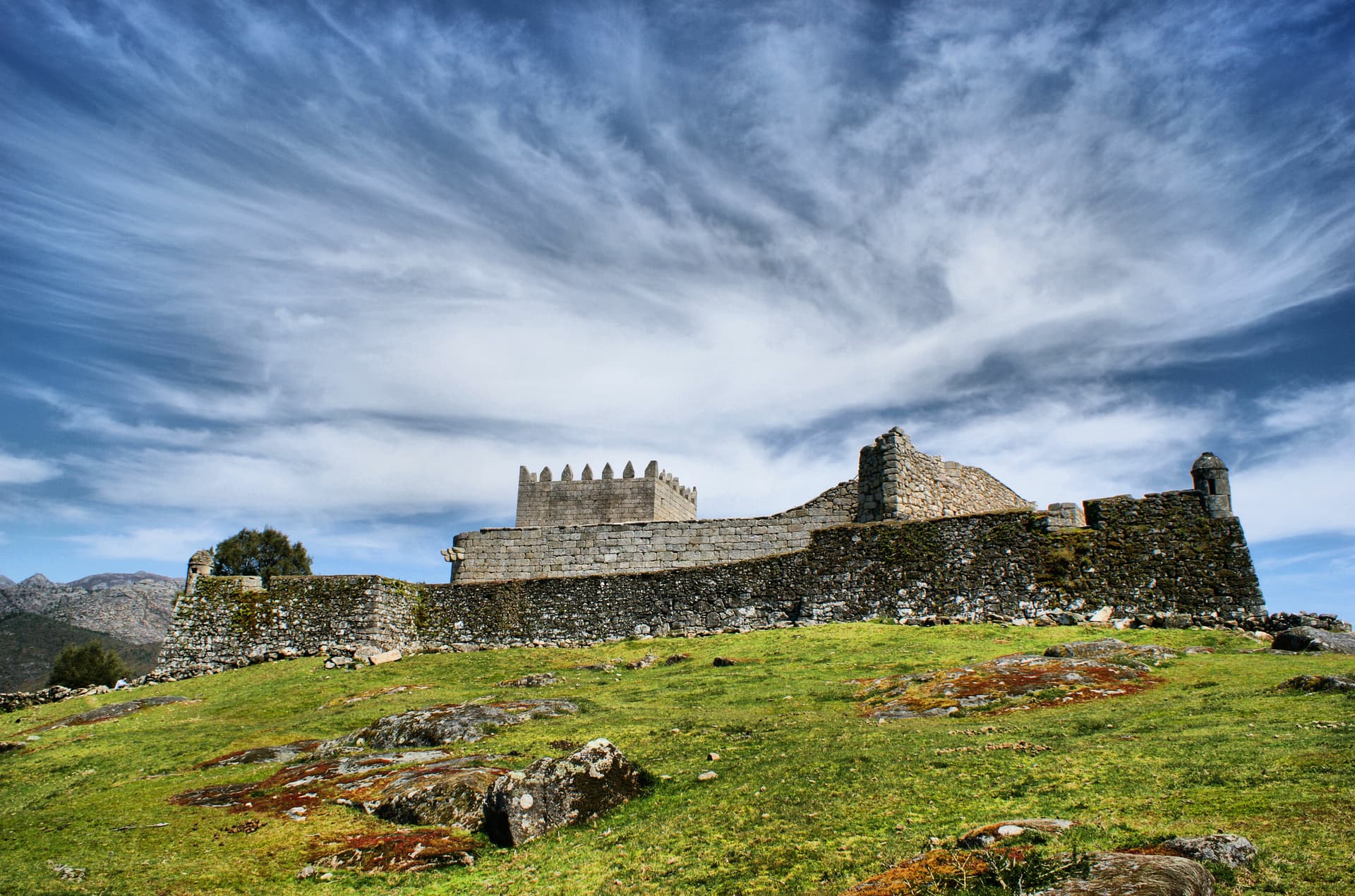 Castle of Lindoso ruins on a grassy hill under a dramatic blue sky in North Portugal.
