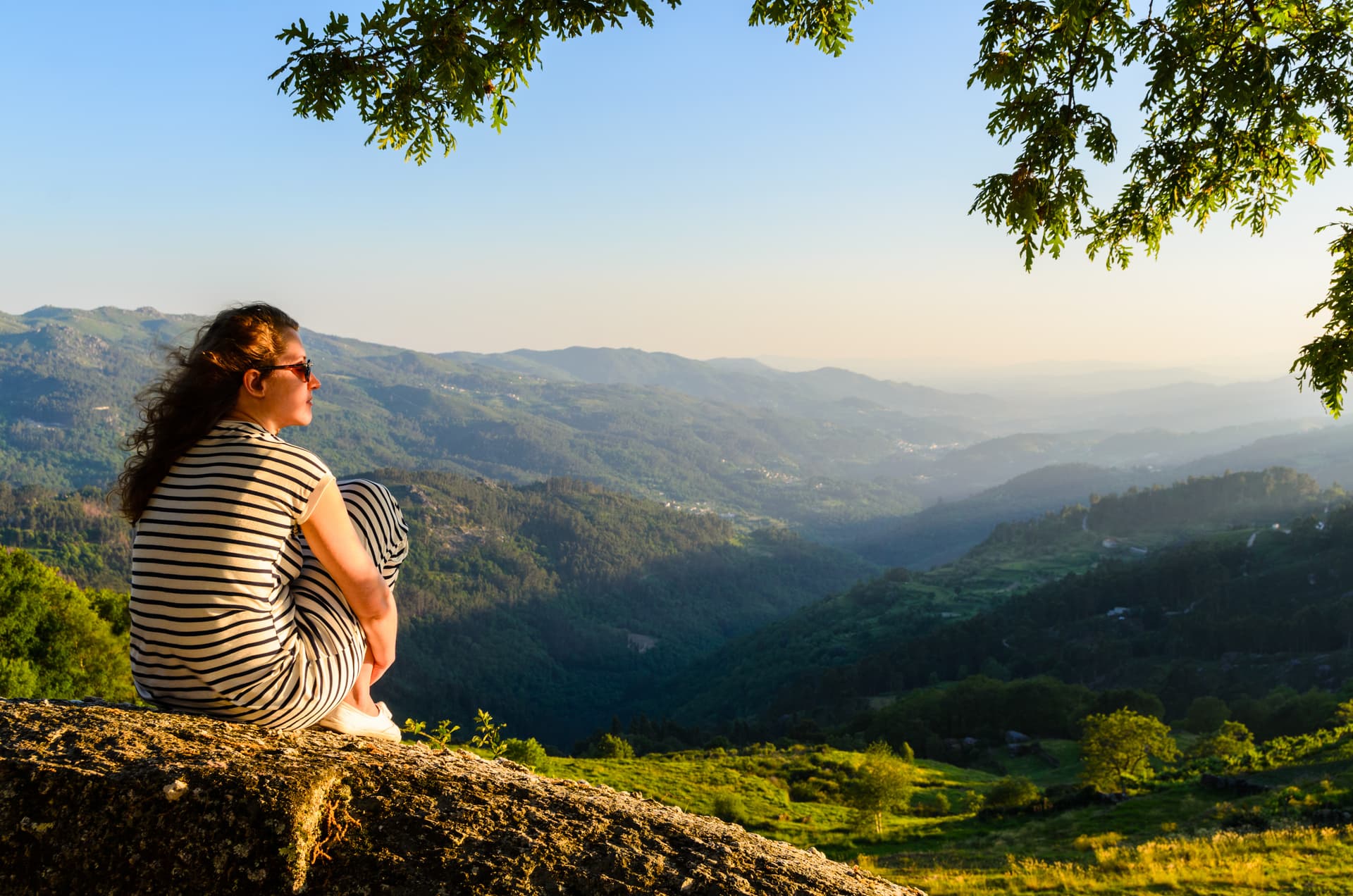 Woman observing lush green mountains from a rocky outcrop in Peneda-Gerês National Park.