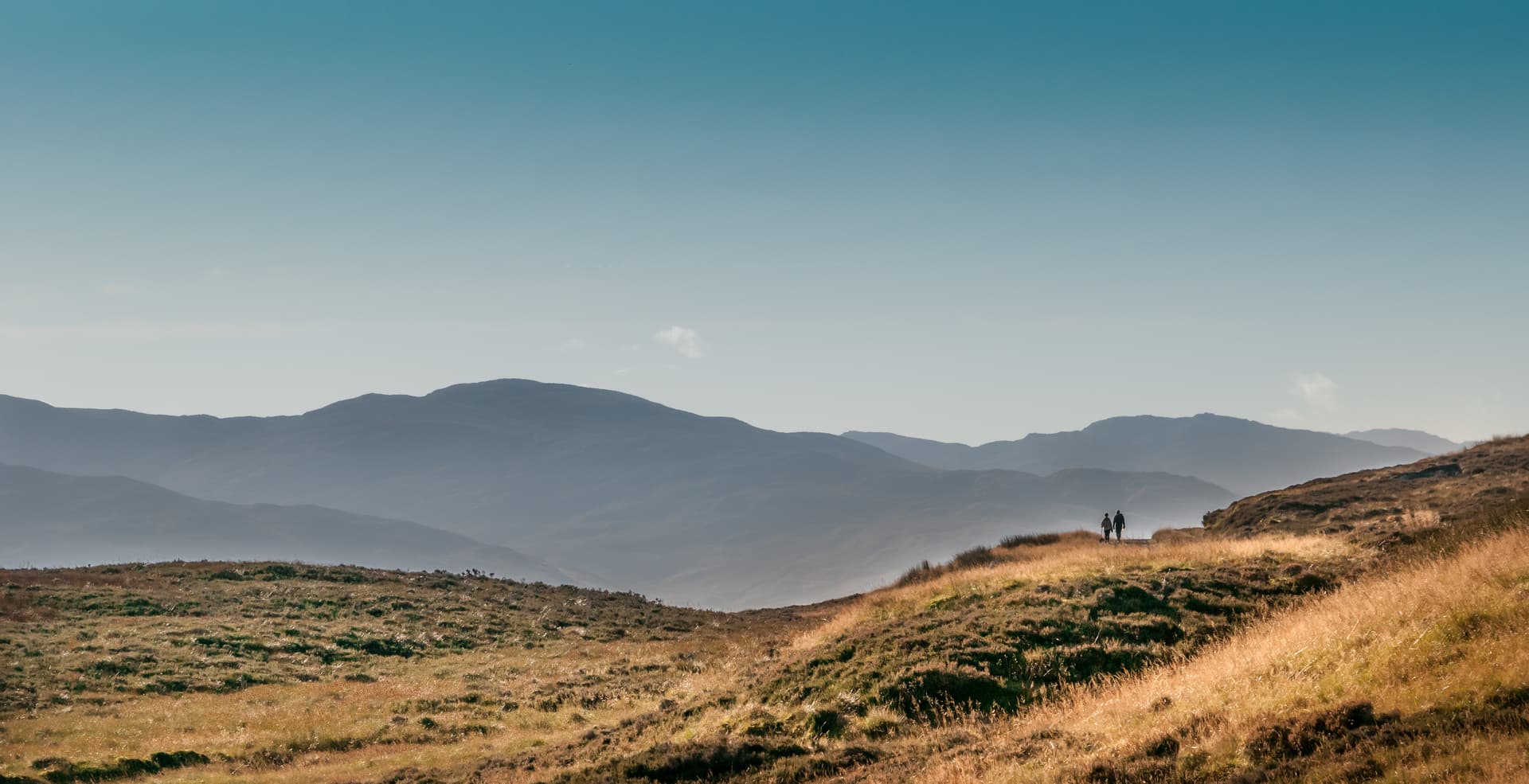 Hikers on grassy hillside with layered mountains in background, Ben Lawers range.