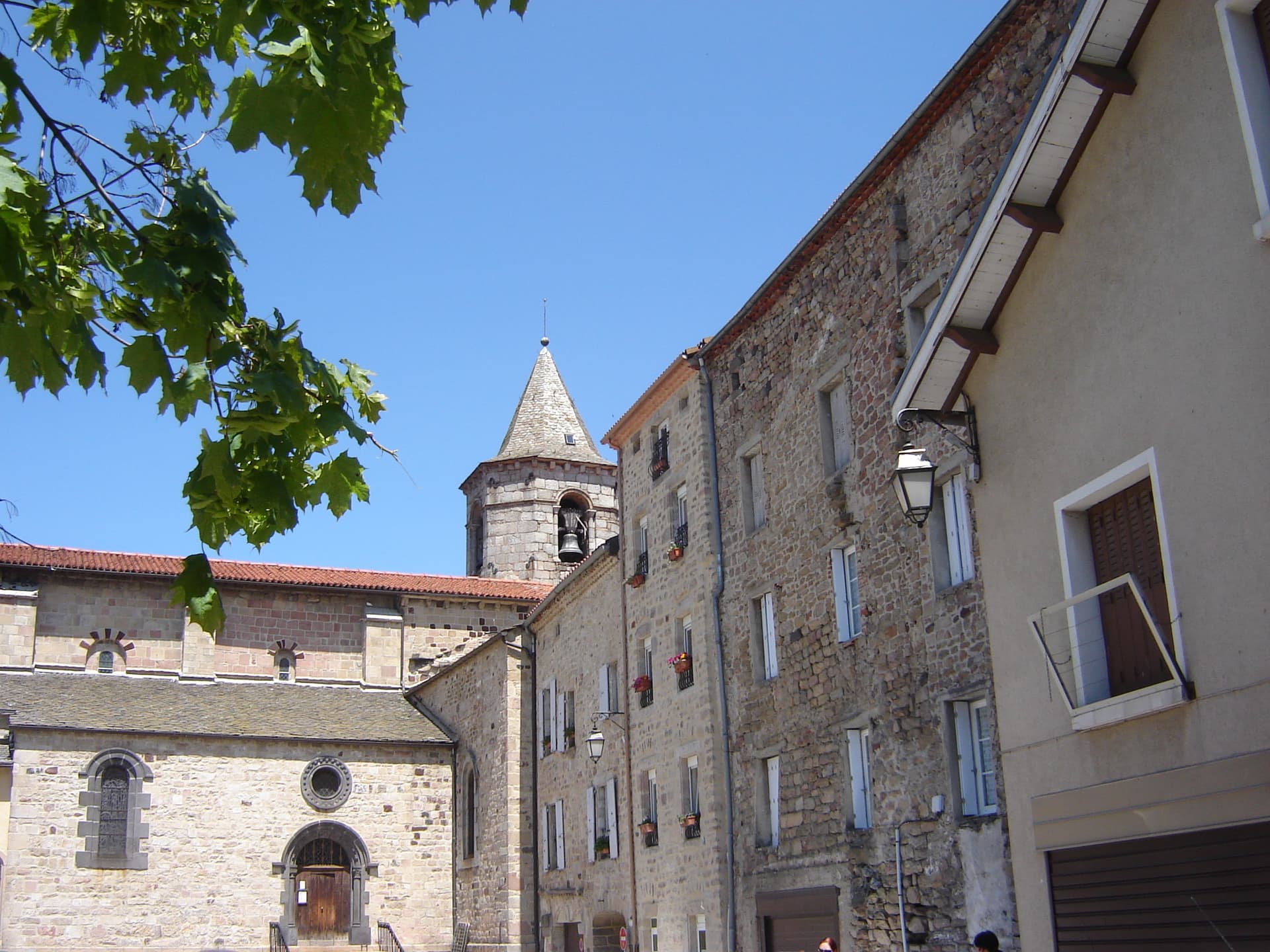 Stone buildings and church tower in Langogne under a clear blue sky with maple leaves.