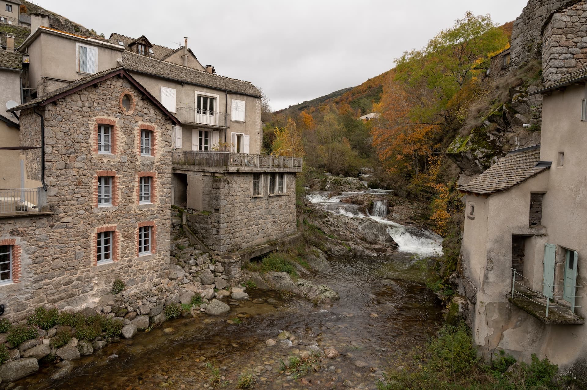 Stone houses along a river with small waterfalls in Pont-de-Montvert village.