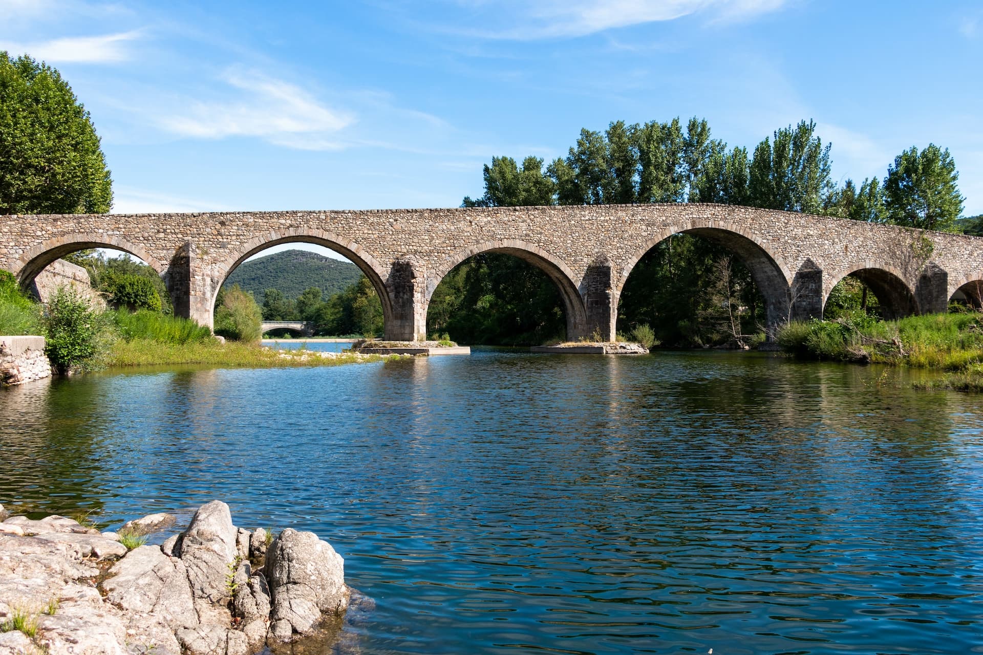 Stone arch bridge over river with lush trees and hills in Saint-Jean-du-Gard