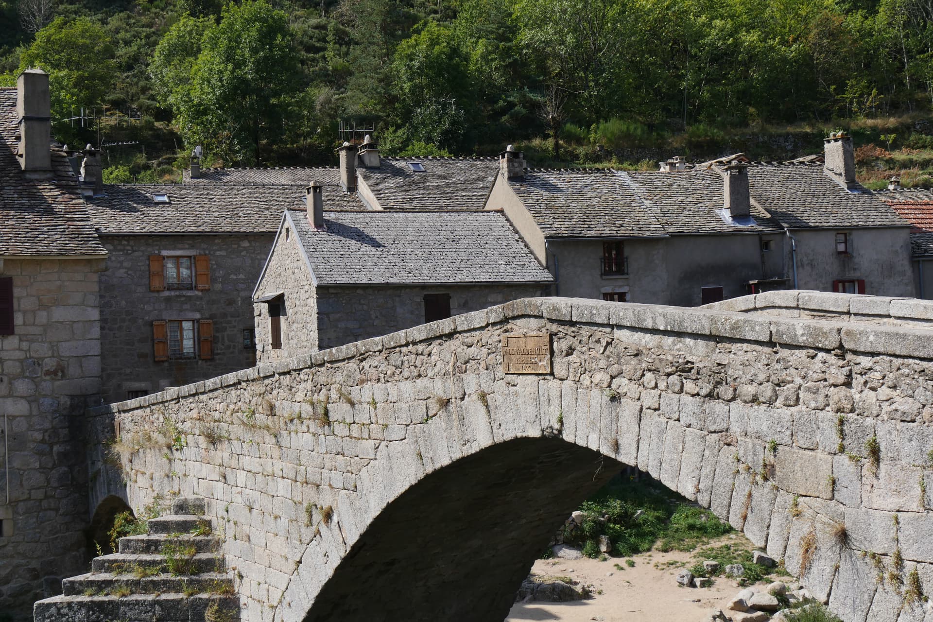 Stone bridge in Pont de Monvert village with slate roofs and forested hillside.
