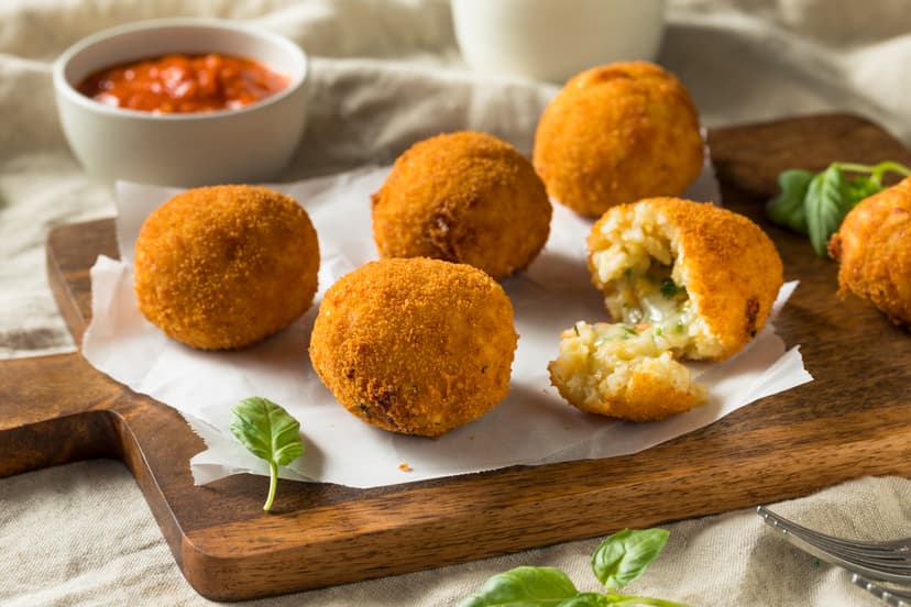 Fried arancini rice balls with cheese filling and dipping sauce on wooden board
