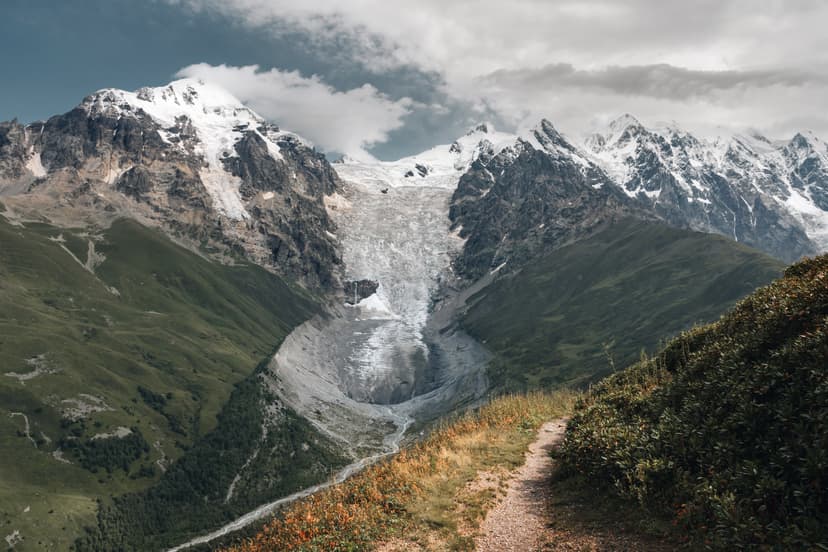 Hiking trail leading through alpine landscape toward snow-capped mountain peaks and a glacier valley