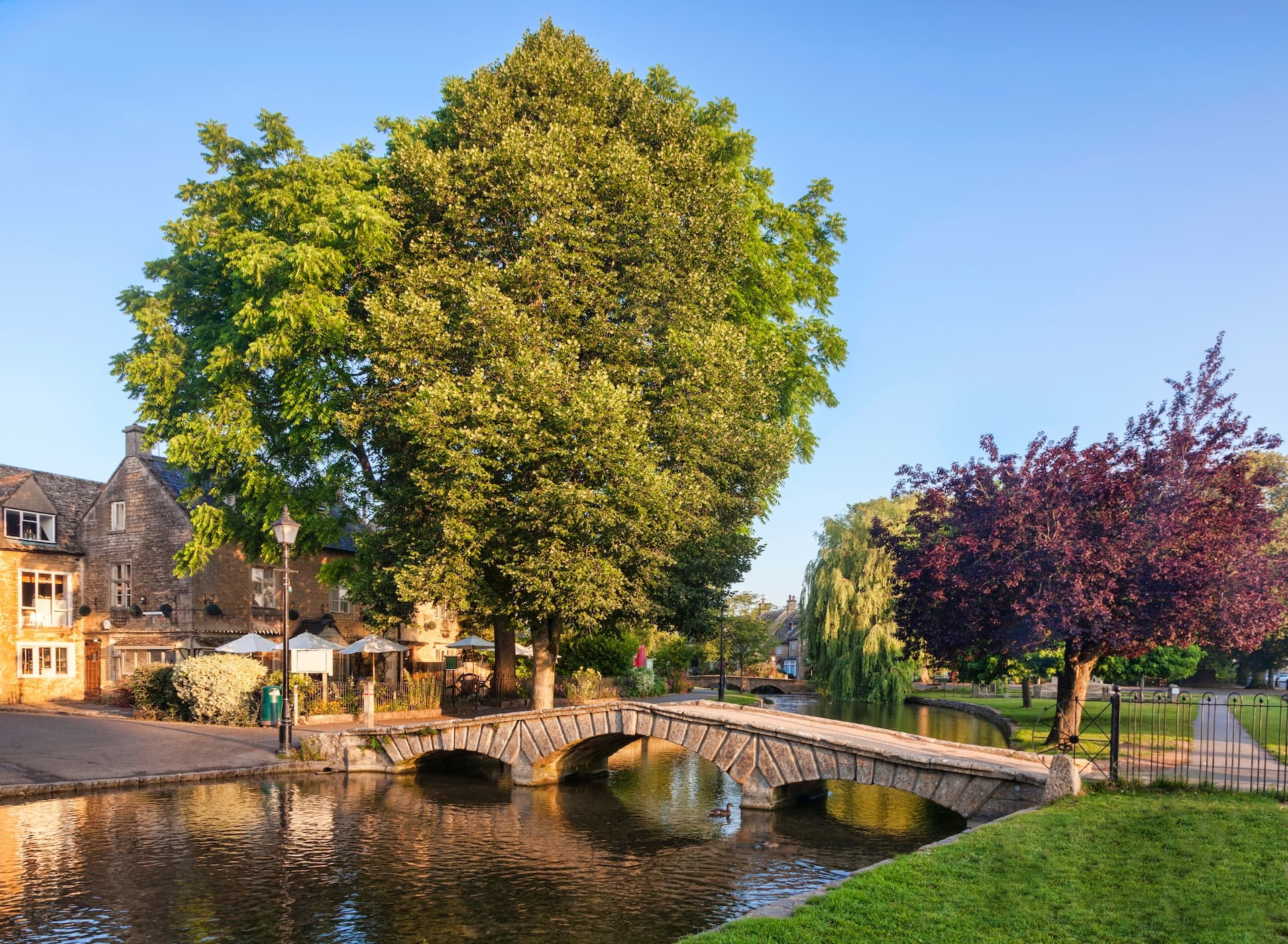 Stone bridge over river in Bourton-on-the-Water, England with large green trees.