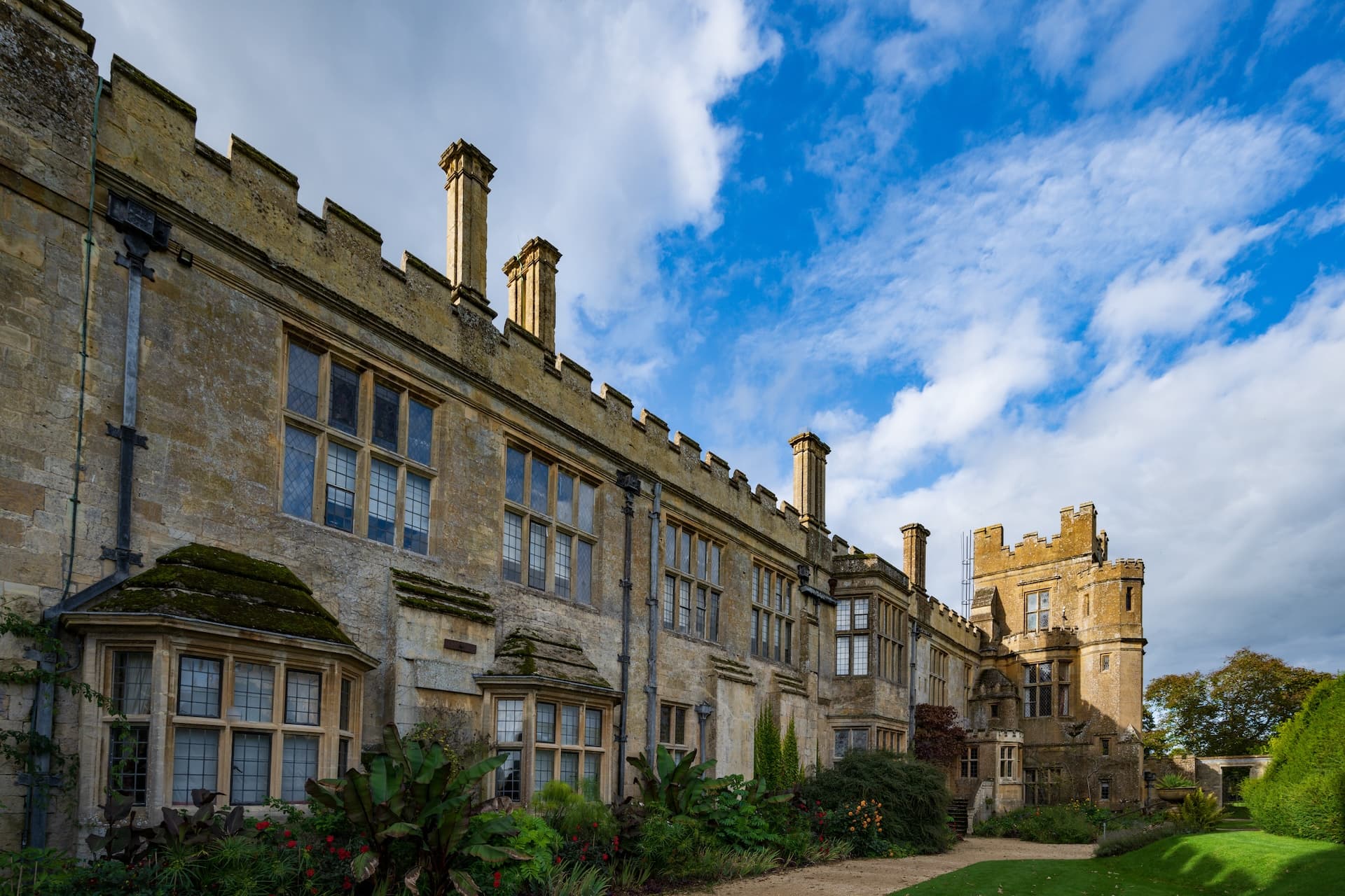 Sudeley Castle in Winchcombe with stone facade, mullioned windows, and blue sky.