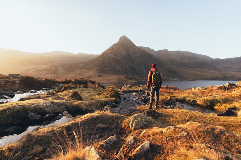 Hiker with backpack standing in mountainous landscape at sunset
