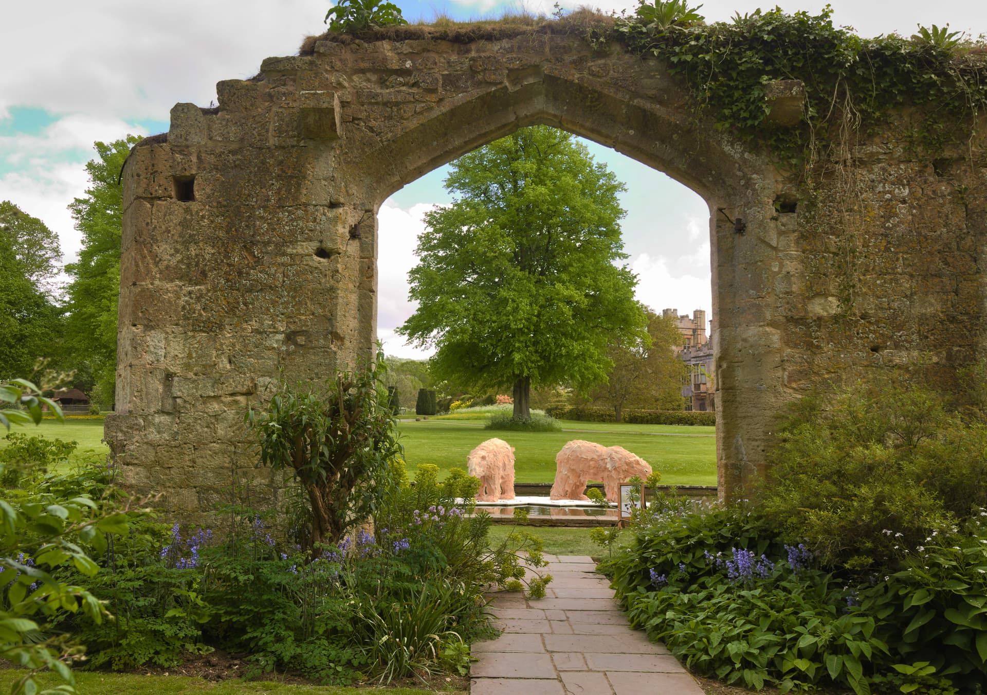 Stone arch ruins framing a lawn with two pink bear sculptures at Sudeley Castle in Winchcombe.