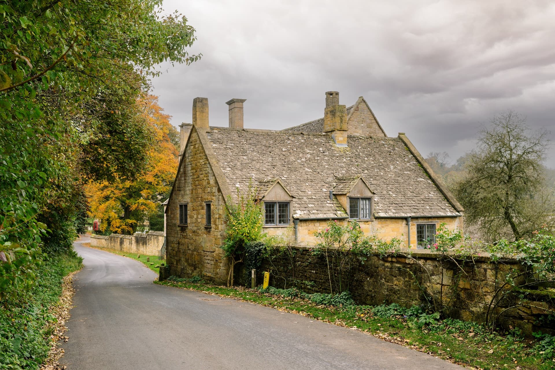 Stone cottage with slate roof on winding road in Broadway, a Cotswold village.
